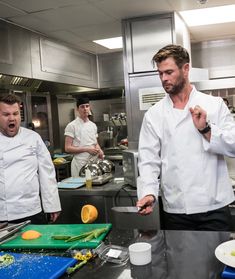 three chefs in a kitchen preparing food on cutting boards with one pointing at the camera