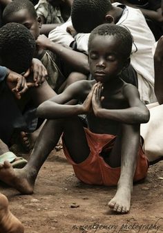 a group of children sitting on the ground with their hands together and looking at something