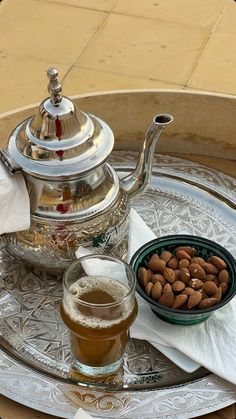 a silver tray topped with a tea pot and bowl filled with nuts