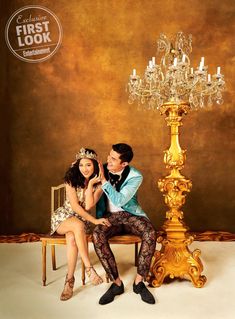 a man and woman sitting on a chair in front of a golden chandelier