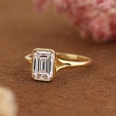 a diamond ring sitting on top of a brown table next to pink flowers and petals