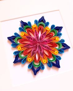 a colorful paper art piece on display in a white frame