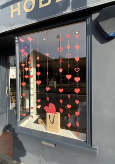 a store front window decorated with red hearts and paper heart garlands hanging from it's windows