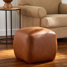 a brown leather ottoman sitting on top of a hard wood floor next to a chair