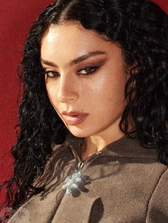 a close up of a person with long black hair wearing a brown shirt and silver necklace