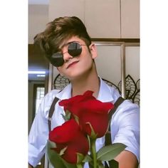 a young man with eye glasses holding a bouquet of red roses in front of him