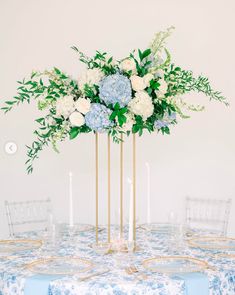 a blue and white floral centerpiece on a table with gold candlesticks for an elegant wedding reception