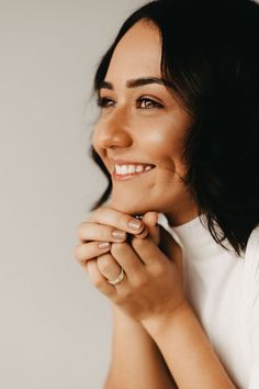 a woman smiling and holding her hands to her chest while wearing a white t - shirt