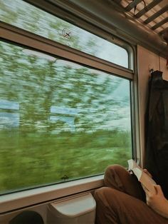 a man sitting on a train looking out the window at grass and trees in the distance