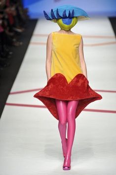 a woman is walking down the runway in a dress with an unusual hat on her head