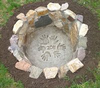 a stone fire pit in the middle of some grass and dirt with hand prints on it