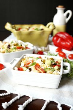 two white dishes filled with pasta salad on top of a table next to chocolate covered cookies