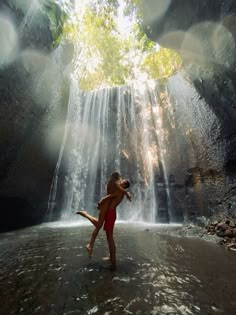 a person standing in front of a waterfall with their arms out to the side while holding onto another person's leg