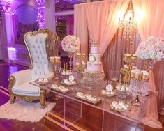 a table topped with lots of cakes and cupcakes next to a chair in front of a window