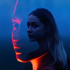 a woman standing next to a man with red light on his face in the dark