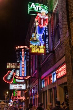 people are walking down the street in front of neon signs and buildings with guitars on them