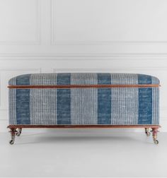 an upholstered bench with wooden legs and blue plaid fabric on the top, in front of a white wall