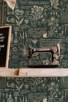 an old sewing machine sitting on top of a wooden shelf next to a wallpaper