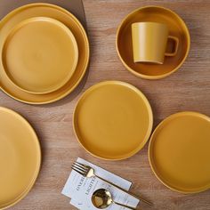 four yellow plates and two cups on a wooden table with a place setting in the middle