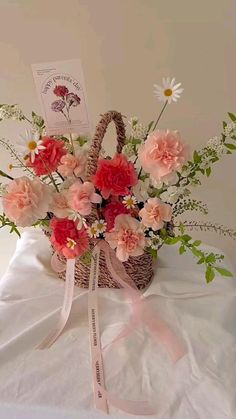 a basket filled with lots of flowers on top of a white table covered in pink ribbon