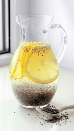 a glass pitcher filled with liquid and topped with lemon wedges next to a spoon