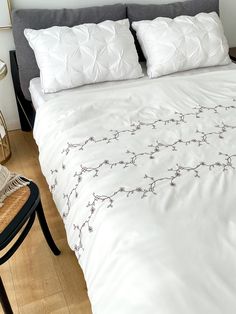 a bed with white sheets and pillows on top of wooden flooring next to a chair