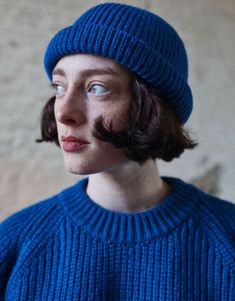 a woman with a moustache wearing a blue sweater and a knitted hat