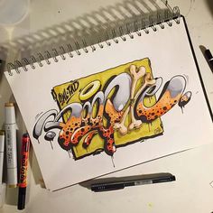 a drawing of some type of graffiti on top of a white table next to markers and pens