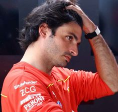 a close up of a person wearing a red shirt and holding his hand to his head