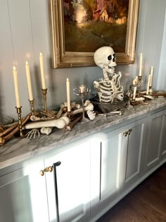 a skeleton sitting on top of a counter next to candles and other items in front of a painting