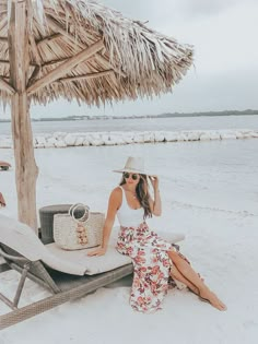 a woman sitting on top of a beach under a straw umbrella