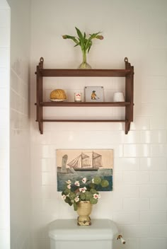 a white toilet sitting in a bathroom next to a wooden shelf with flowers on it