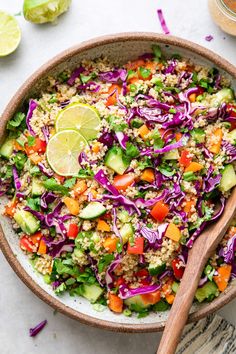 a bowl filled with rice, cucumber, red cabbage and carrots next to a wooden spoon