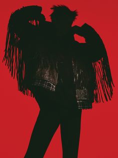 the silhouette of a woman with fringes on her jacket is against a red background