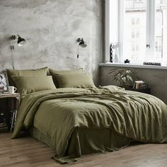 a bed with green sheets and pillows in a room next to a white brick wall