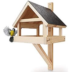 a wooden bird house with a black roof and a yellow finch on the outside side