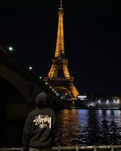 a man standing in front of the eiffel tower at night with his back turned to the camera