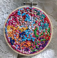 a close up of a colorful embroidery on a white table cloth with a wooden hoop