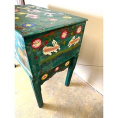 a green painted wooden table with flowers and rabbits on the top, sitting in front of a white wall