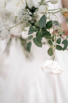 a bouquet of white flowers and greenery is held by a bride's hand