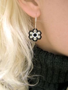 a woman wearing black and white beaded earrings with flower design on the back of her ear