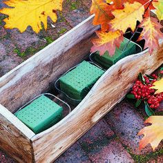 a wooden box filled with containers next to autumn leaves