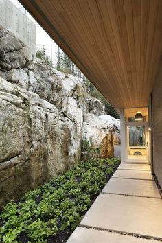 the walkway is lined with green plants and large rocks on either side of the house