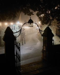 a foggy street at night with an iron gate and lamp post in the foreground