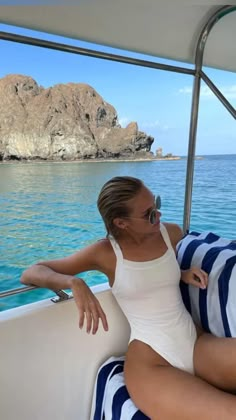 a woman sitting on the back of a boat in the ocean next to a rock formation