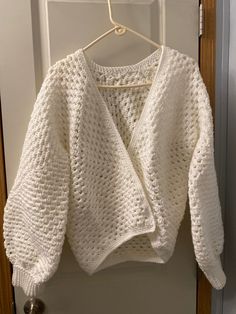 a white knitted sweater hanging on a hanger in front of a door handle