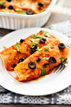 an enchilada with black olives and parsley on a white plate