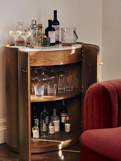 a bar with liquor bottles and glasses on it next to a red chair in a room