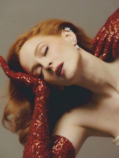 a woman in red sequins is posing with her hands on her face and arms behind her head