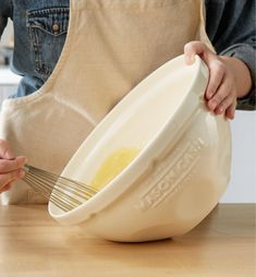 a person holding a whisk in front of a bowl on top of a wooden table